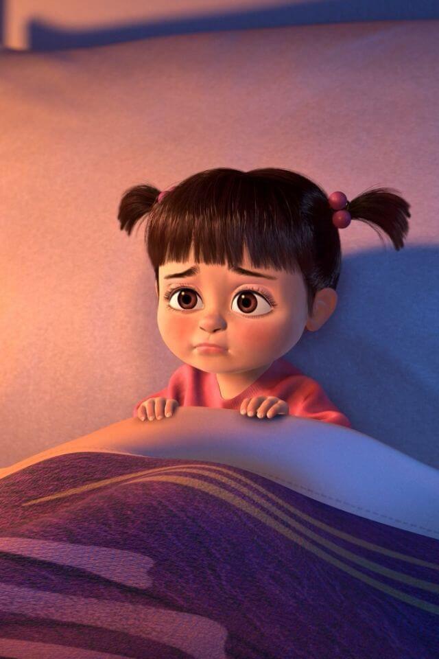 Personagem Boo de Monstros S.A., animação da Pixar, sentada em sua cama com coberta, olhando com medo